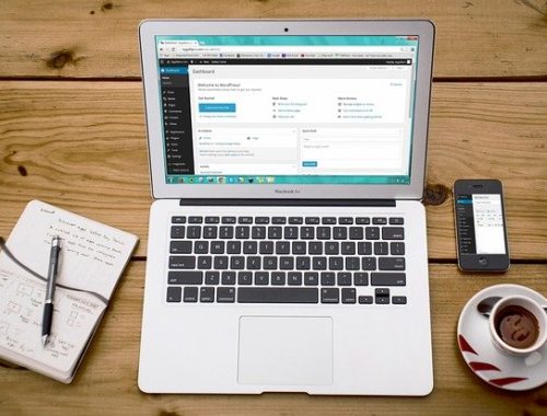 Photo of laptop with wordpress dashboard on screen, cup of tea and notebook with a pen